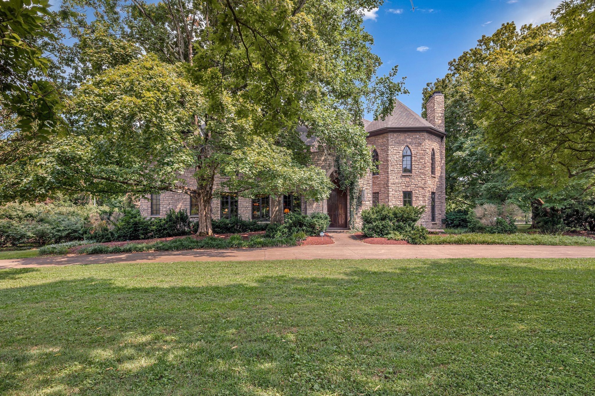Front exterior of 1108 Belle Meade Boulevard, a stone home with a tower seen across a wide lawn and mature trees, one of the Belle Meade homes for sale in Nashville