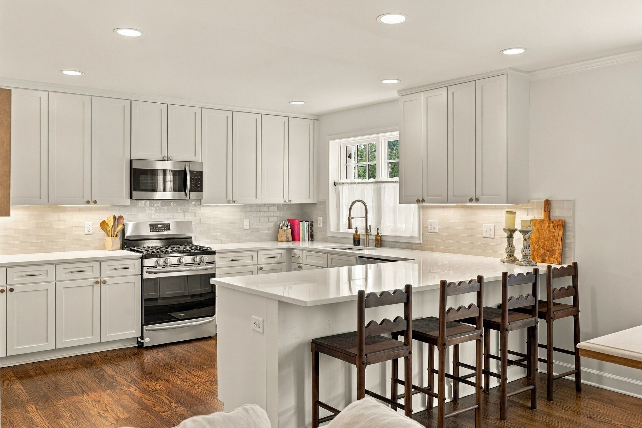 Renovated white kitchen with quartz counters, stainless appliances and a peninsula with seating at 200 Leake Avenue in Belle Meade Nashville