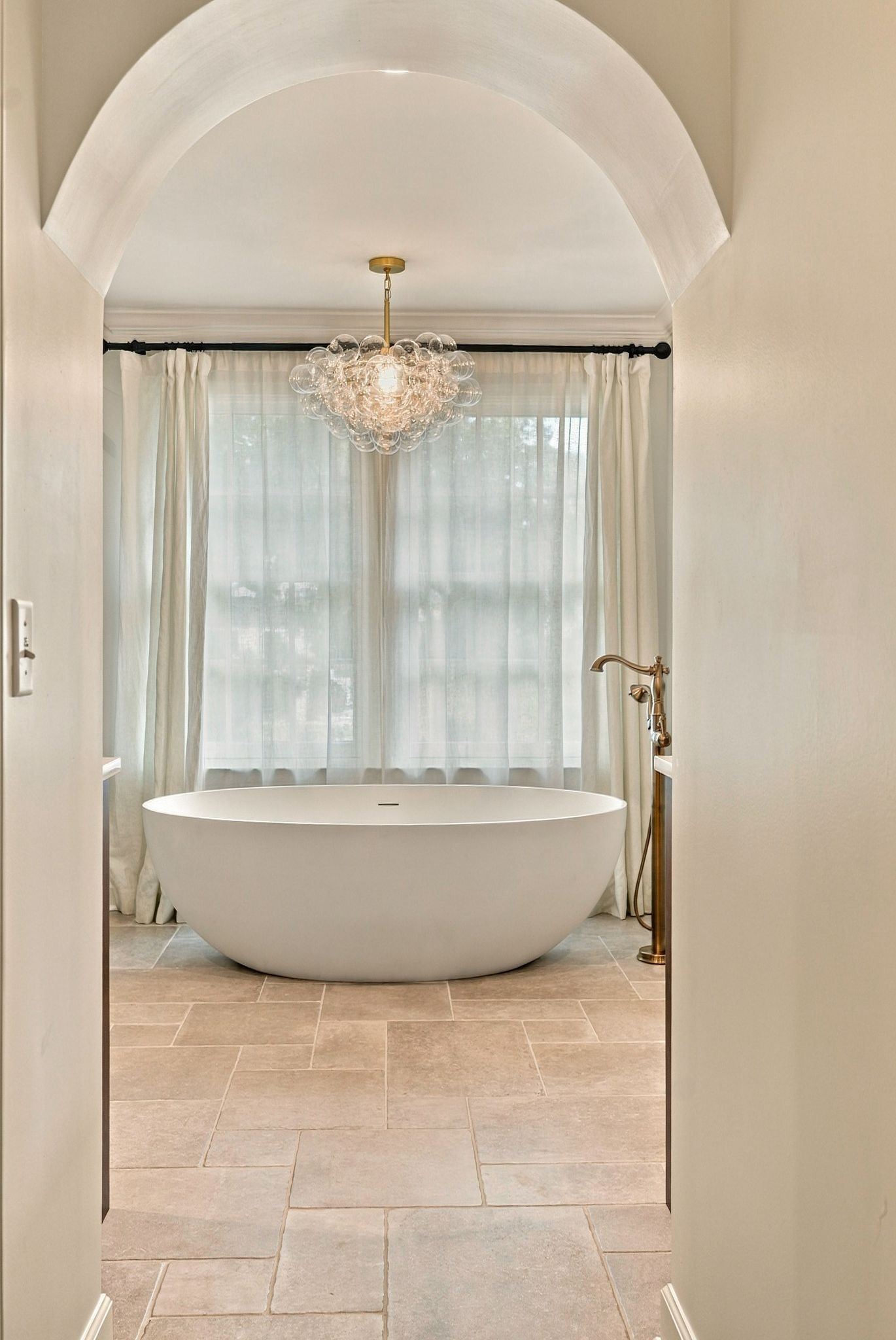 Primary bath with a freestanding soaking tub framed by windows under a glass bubble chandelier at 200 Leake Avenue in Belle Meade Nashville
