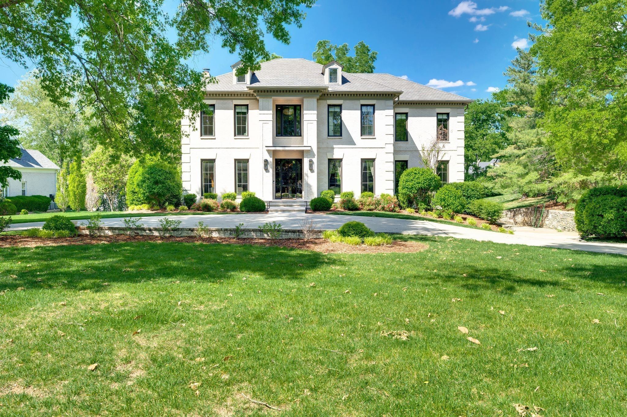Front exterior of 4304 Warner Place, a white two story home with black windows, a front lawn and large trees, one of the Belle Meade homes for sale in Nashville