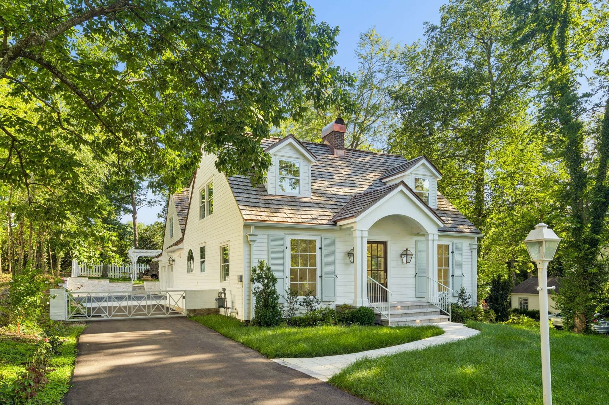 Front exterior of 4401 Iroquois Avenue, a white Cape Cod home with dormers, a cedar shake roof and a front lawn, one of the Belle Meade homes for sale in Nashville
